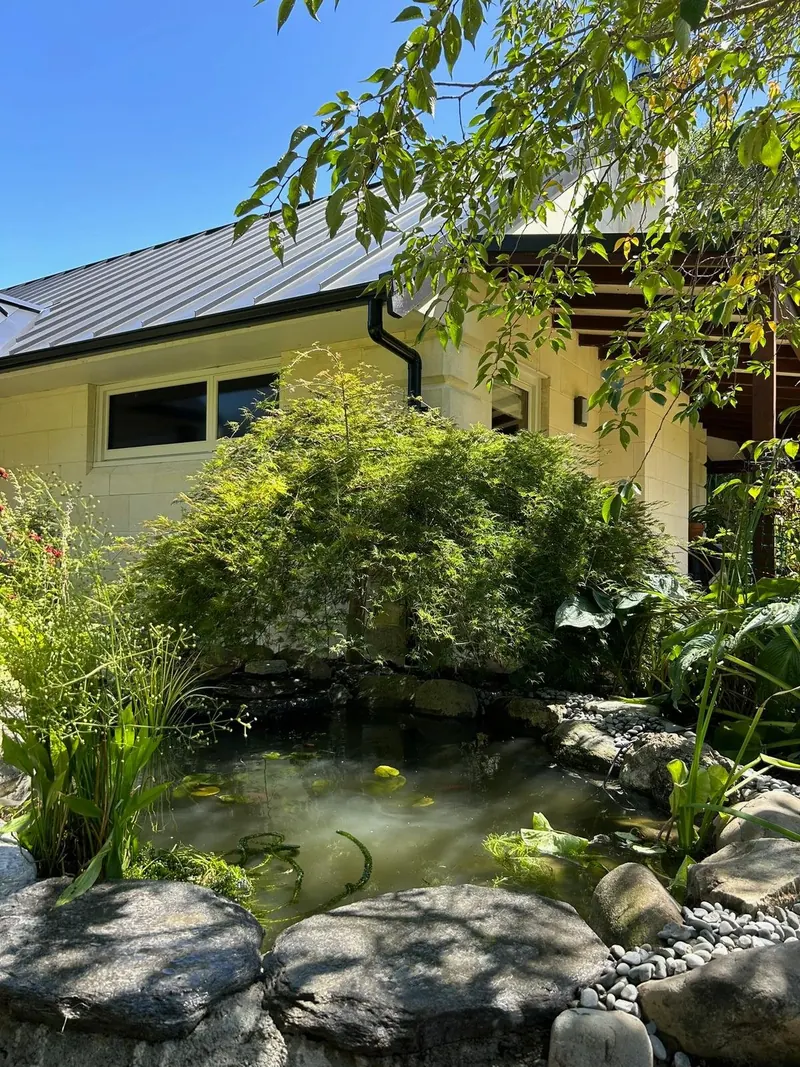 Residential pond with stone edging and planting in front of a house with a metal roof